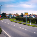 (C) DL Fotografie - Daniel Löwedey
Mit freundlicher Genehmigung der Stadtwerke Frankenthal Ortseinfahrt mit Heßheim-Ortsschild, kurviger Straße, Häusern und Windrädern im Hintergrund.