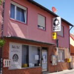Straßenszene mit der Bäckerei Raab, Postfiliale und bunten Wohnhäusern in Heßheim